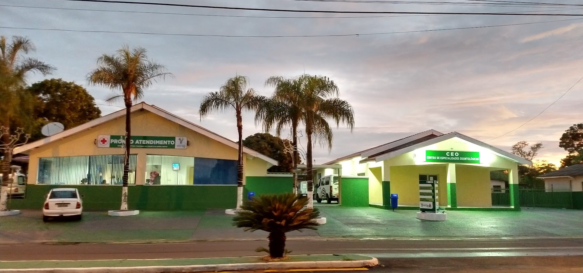 Fachada da Santa Casa de Quintana ao entardecer, com a entrada do Pronto Atendimento à esquerda e o Centro de Especialidades Odontológicas à direita, entre palmeiras.